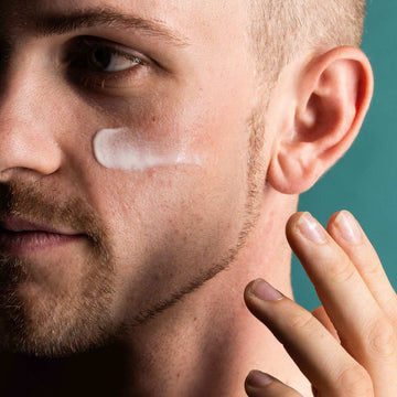 Man applying cream to his face with a teal background